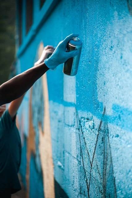 Street Art Wien - eine Hand, die eine Spraydose hält und eine Wand blau besprüht